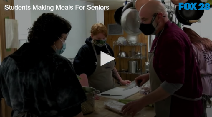 3 people standing around a prep table preparing food