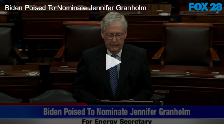 man standing in conference room with text on screen readin "Biden poised to Nominate Jennifer Granholm for Energy Secretary"